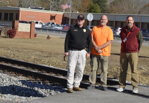 Showing the close proximity of the Norfolk Southern railroad tracks to Phillips schools in Bear Creek, are, from left, Bear Creek Police Chief Eddie Collins, Mayor Rob Taylor and High School Principal Dr. Al Temple. They are standing on the railroad tracks.
